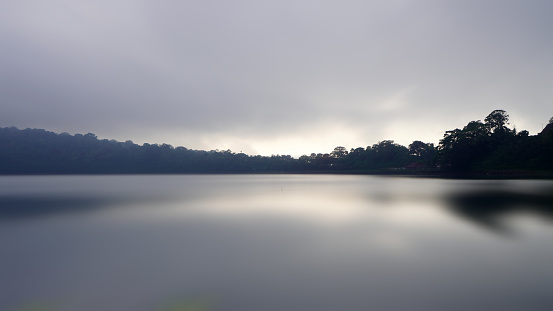 Tranquil lake view with gray cloudy sky, calm and smooth water reflection. Lake nature landscape background. Natural backgrounds.