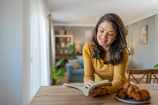 Photo of young beautiful woman reading a book and having breakfast