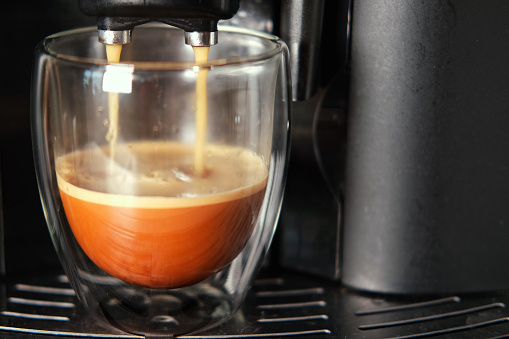 Espresso Pouring from Coffee Machine into Transparent Double Wall Glass Cup. Preparing Fresh Black Americano. Morning Coffee Brewing Preparation. Professional Electric Automatic Kitchen Coffee-Maker. 4K Pouring black coffee into white ceramic cup. Front view. Close up. Hot coffee drink pour into cup. Freshly brewed Espresso, americano. Coffee mug closeup. household appliances