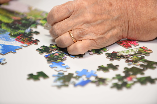 A senior woman with dementia is training by picking up pieces of a jigsaw puzzle.