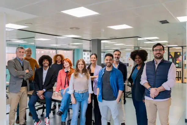 A diverse group of professionals smiling and posing together in a contemporary coworking office space.