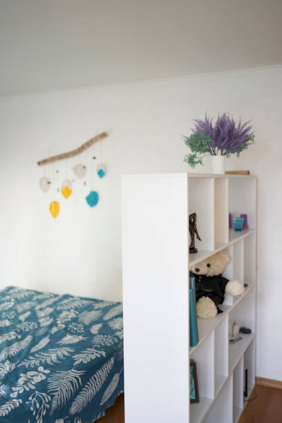 white shelf divides the room into two parts, separating the work area from the bed