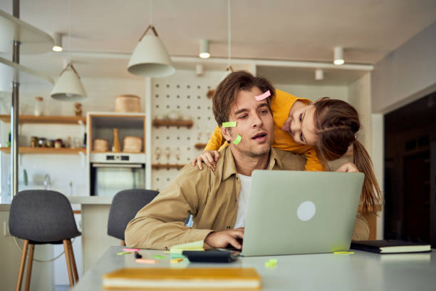 istock A little girl makes faces and distracts her stressed father from remote work at home. 2025053274