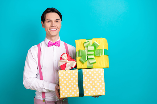 Photo portrait of pretty young male hold gift boxes pile receive dressed stylish pink outfit isolated on aquamarine color background.