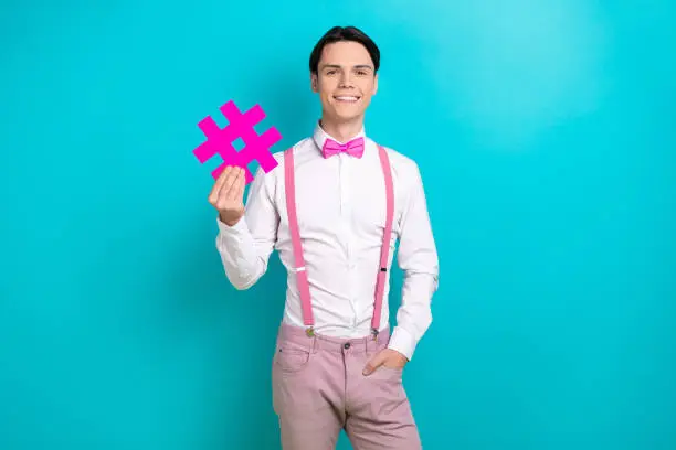 Photo of Photo portrait of pretty young male hold hashtag number symbol wear trendy pink outfit isolated on cyan color background