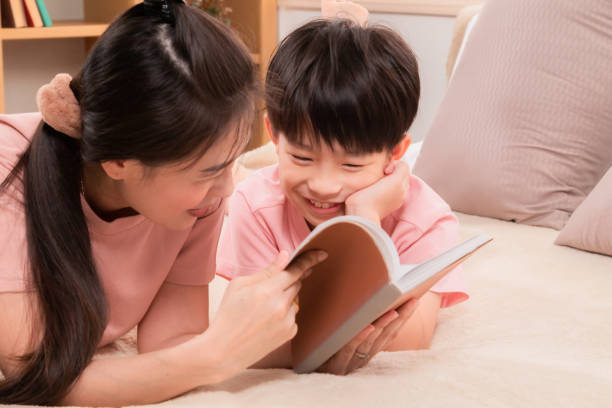 istock Asian happy elementary school kid and single mom spend free time reading a book and tease in holiday. Beautiful mother telling fairy tale stories to adorable son laying on bed, parenthood relationship 2025085579