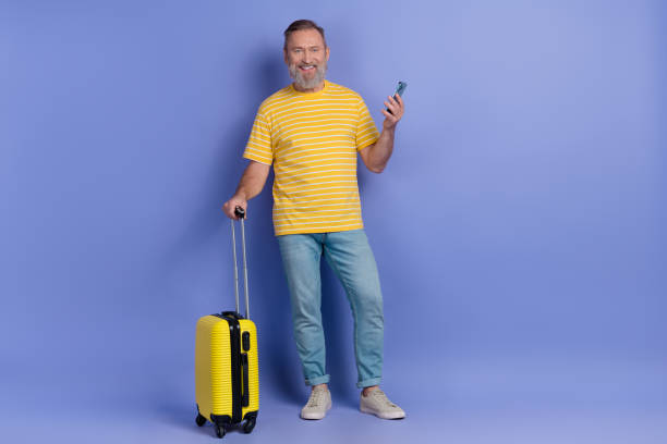 istock Full size photo handsome person hold suitcase use smart phone empty space isolated on violet color background 2025087711