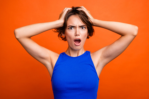 Photo of stressed shocked girl dressed blue top arms head open mouth isolated orange color background.