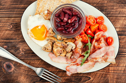 Fried bacon and eggs, toast and beans on rustic wooden table. Traditional English breakfast. Top view, flat lay.