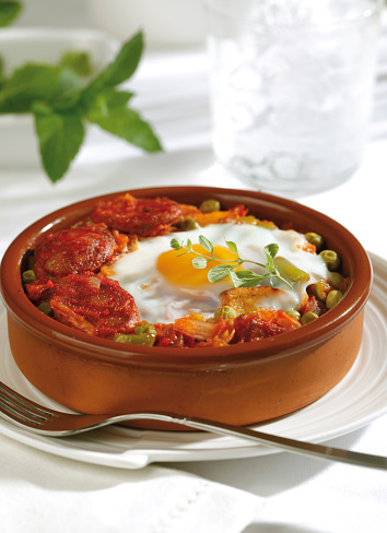 Baked eggs with chorizo and vegetables in a clay pot. Spanish food, flamenco eggs