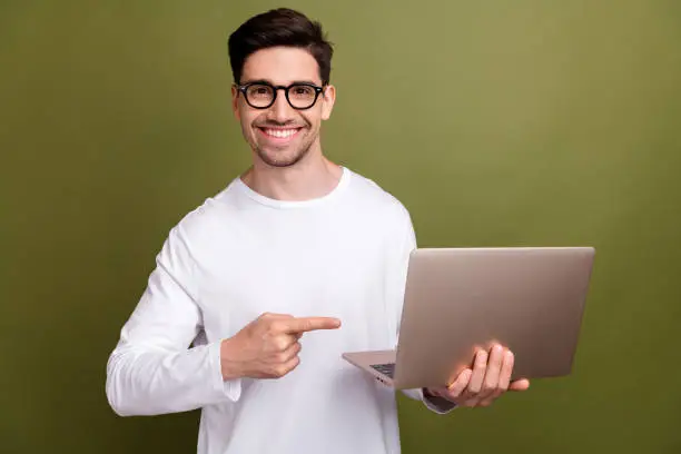 Photo of Photo of young optimistic operations manager specialist directing finger to his new apple macbook pro isolated on khaki color background