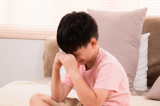 Asian adorable boy crying on bed because he didn't go out to play with his friends on holiday. young children making mistakenly crying in bedroom. son scolded by mother.