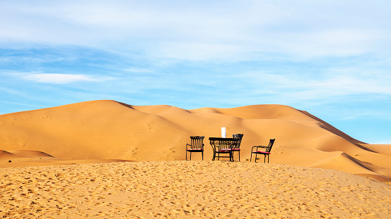 Classic chairs and table set in the dunes of the Moroccan desert, romantic and fantasy concept. Panoramica.