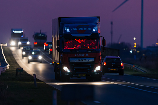 Netherlands, South Holland, Zuidplas, Zevenhuizen, February 9th 2023, red Dutch 2019 DAF CF truck with red  illuminated cabin and other traffic (cars, van and trucks) driving on the N219 road at Zevenhuizen just before sunrise, the DAF CF is made by Dutch manufacturer DAF Trucks NV since 1992