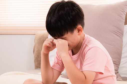 Asian adorable boy crying on bed because he didn't go out to play with his friends on holiday. young children making mistakenly crying in bedroom. son scolded by mother.