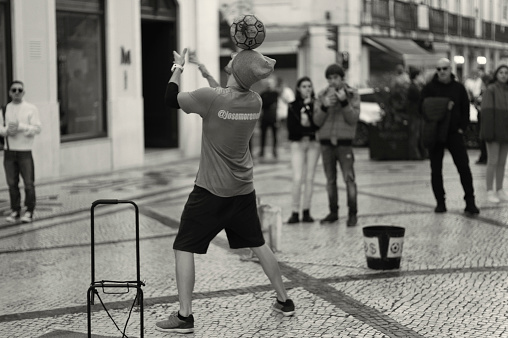 Lisbon, Portugal - November 11, 2023: A street artist performs a juggling act with a soccer ball at the Rua Augusta street in Lisbon downtown.