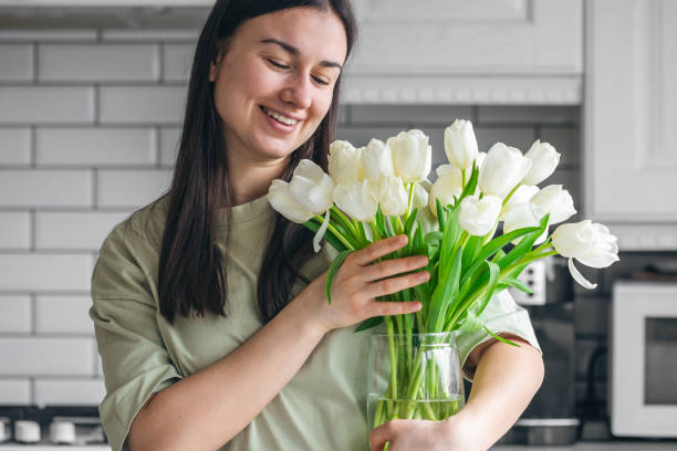 istock A woman holds a vase with white tulips in a kitchen interior. 2025164255