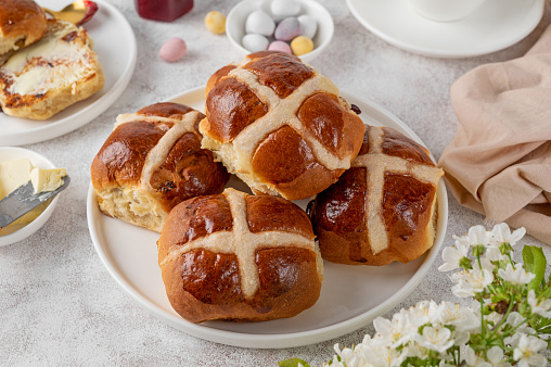 Traditional Easter hot cross buns on a white plate with butter, berry jam and cup of tea. Delicious Easter breakfast
