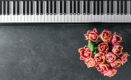 Piano keyboard and a bouquet of flowers on a dark textured background, top view. Copy space.