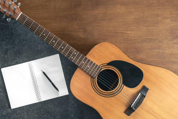 istock Acoustic guitar and notebook on a textured black and wooden background. 2025169666