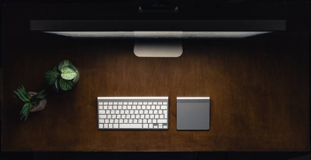 Computer, keyboard and cup of tea on a wooden table at night, top view. Workplace in an office in a dark room. Night work concept.