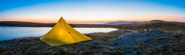 istock Yellow tent illuminated at sunrise by idyllic mountain lake panorama 2025199655