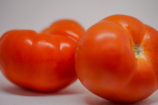two tomatoes, ripe but healthy and shiny, on a white background