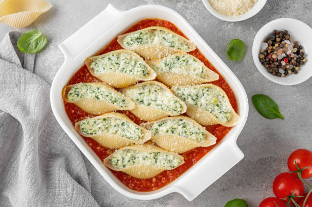 istock Conchiglioni pasta stuffed ricotta cheese and spinach with tomato sauce in a white baking dish on a gray concrete background. 2025215006