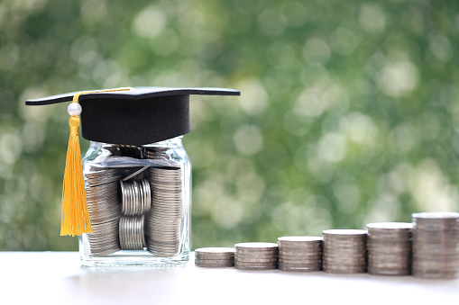 Graduation hat on coins money in the glass bottle on natural green background, Saving money for education concept