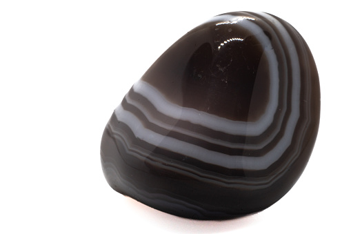 Small shiny polished Botswana Agate Chalcedony, a colorful distinctly layered crystal with white, brown and black bands. Banded Agate tumbled stone on white surface isolated
