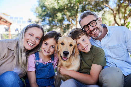 Portrait of smiling parents and their two young children loving their golden retriever while sitting together outside in their yard in summer