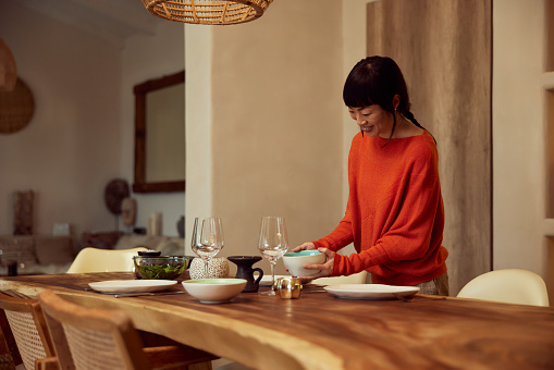A happy Asian female, serving a table for dinner, waiting for her friends.
