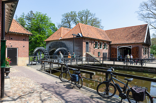 An old historic watermill on the banks of a river. The small waterfall blurs in the long exposure. Trees and plants in the background.