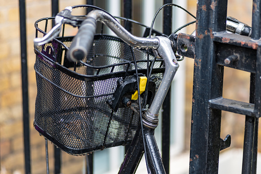 A old bicycle with a front basket chained to a fence railing.
