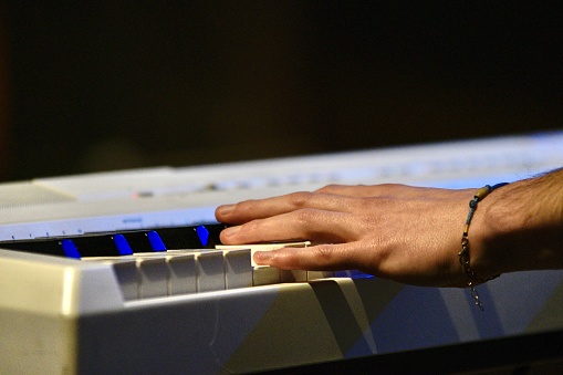 Hand on keyboard, musician playing piano on stage closeup