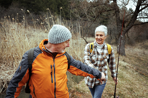 A senior couple enjoys a leisurely walk, each carrying fishing poles