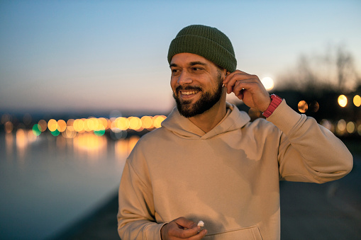 Portrait of a Young Bearded Male Athlete With in Wireless Headphones Outdoors in City at Night. Sporty Style.