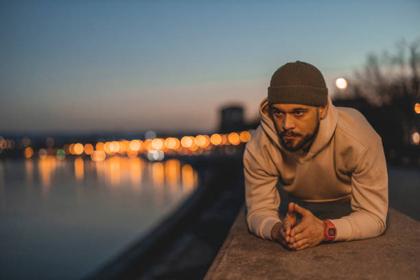 Strong Fitness Man in Athletic Workout Clothes is Doing a Plank Exercise Outdoors at Night. Background With Bokeh Lights