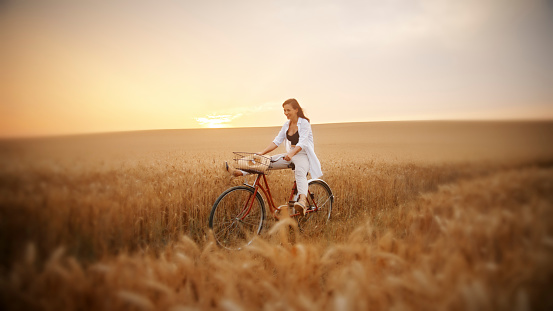 Happy Woman Enjoying Riding Her Bicycle Through A Wheat Field. Each Time She Pedals, She's Fully Embracing The Simple Joy Of The Moment, Being Carefree, And Loving The Beauty Of Nature Around Her