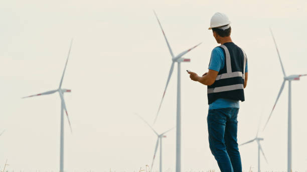 istock Male Engineer Using Mobile Phone Towards Wind Turbines against Sky 2025390278