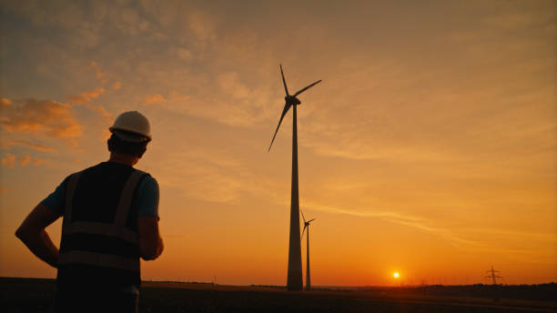 istock Male Engineer Running towards Wind Turbines against Orange Dramatic Sky at Sunset 2025394073