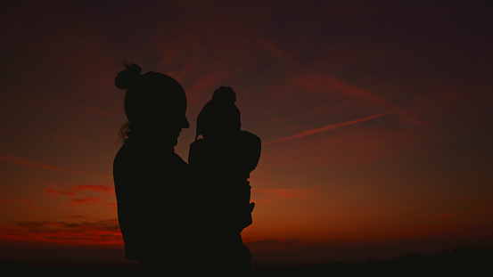 Silhouetted against the Orange Sky During Sunset,a Mother Carries Her Baby,Embodying Love and Protection in a Serene and Picturesque Moment of Tranquility.