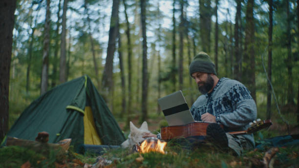 istock Man Working on Laptop while Sitting in Front of Campfire at Forest during Vacation 2025398938