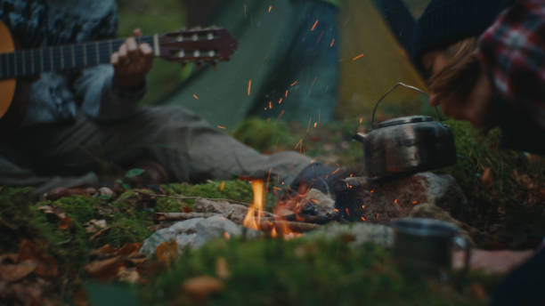 istock Woman Setting Up Fire while Man Playing Guitar in Forest during Vacation 2025404362