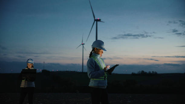 istock Female Engineers in Work Attire Examining Wind Turbines with Technology on Farm at Dusk 2025408762