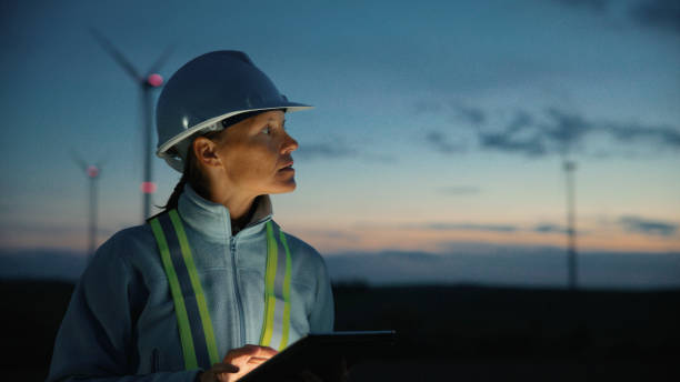 Engineer Woman Checking Wind Turbines on Tablet at Dusk