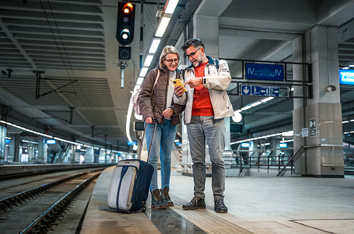 Cheerful mature couple using phone while waiting for a train