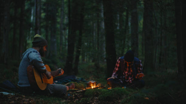istock Man Playing Guitar while Woman Sitting near Campfire Surrounded with Trees in Forest 2025409310