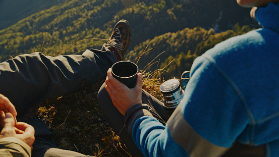 Couple Sitting on Mountain Peak,Basking in Sunlight,Savoring Tea as They Gazing at the Picturesque Landscape Below,Their Faces Filled With Contentment and Joy.