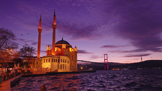 As Twilight Descends,The Illuminated Ortakoy Mosque and Bosphorus Bridge Stand in Stunning Contrast against the Backdrop of a Cloudy Sky by the Sea. This Enchanting Scene Captures the Timeless Beauty of Istanbul's Skyline,Where Architectural Marvels and Natural Elements Blend Seamlessly at Istanbul,Turkey